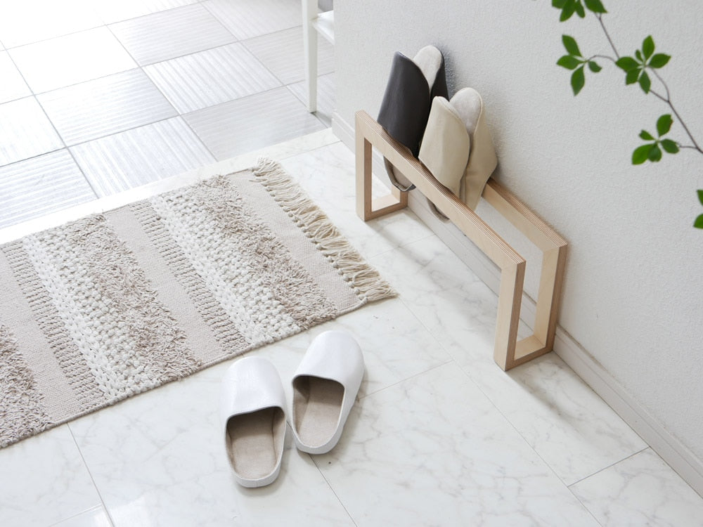 ブランド「sarasa design」のプレーンステッチルームシューズがグレーの木製フローリングの上に置かれている様子。