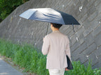 灰色のマブワイドライト遮光ミニ65傘をさして雨と風の中を歩く人