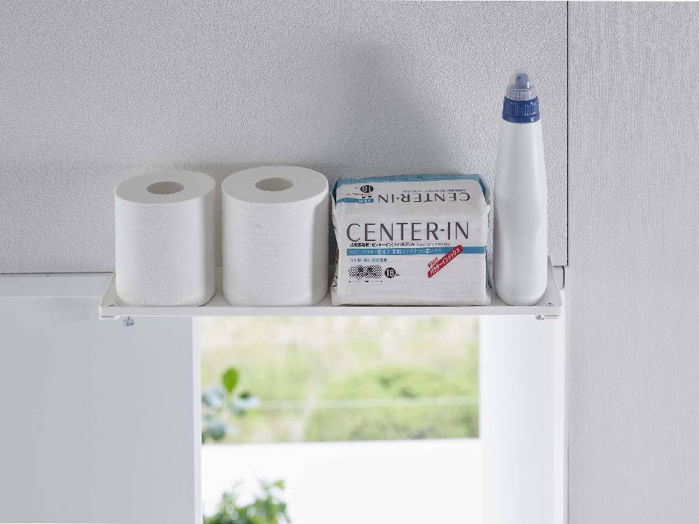 towerタワーの鴨居上神棚 W45が浴室の棚に取り付けられ、トイレットペーパーやペーパータオルが整然と配置されている様子
