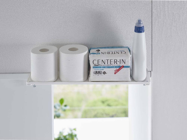 towerタワーの鴨居上神棚 W45が浴室の棚に取り付けられ、トイレットペーパーやペーパータオルが整然と配置されている様子