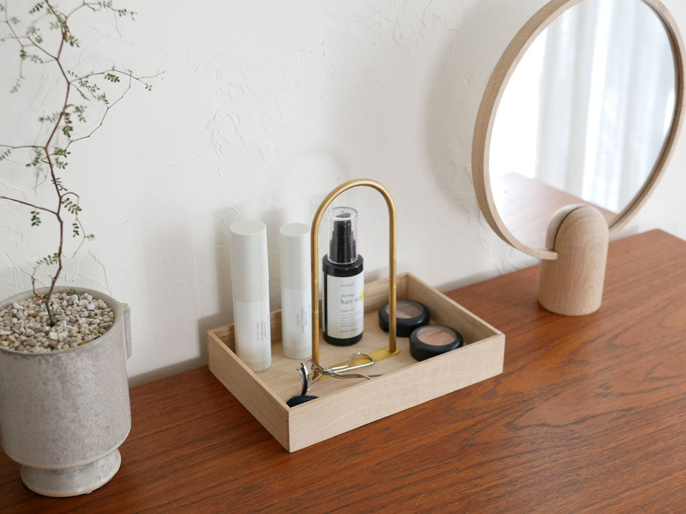 フリッツ・ハンセン製Skagerak Norr Carrier。オーク材と真鍮メッキ仕上げスチールを使用したオフィスデスク上に配置され、文房具やコスメ、ハウスプラントが整理されている様子