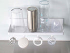 白色のフィルムフックトレーW30がキッチンの棚に取り付けられ、プラスチック製の調理器具や蓋を整理している様子