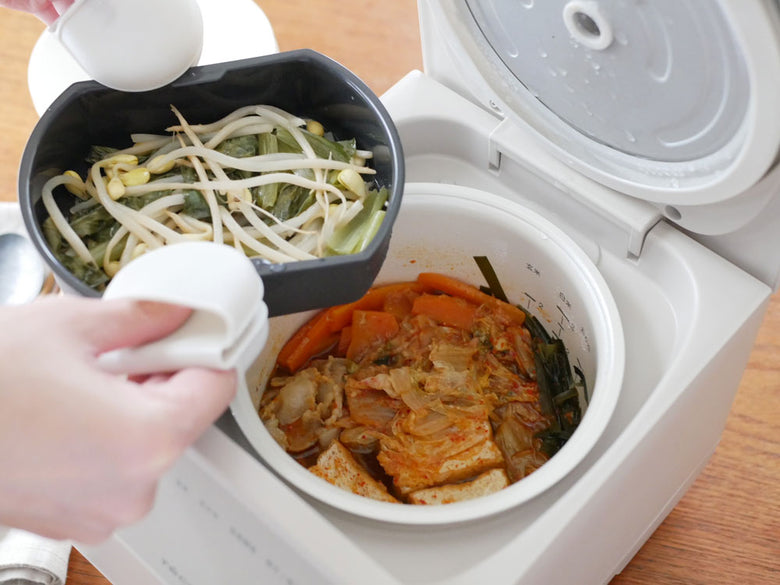 récolteクッキングライスクッカーと調理中の料理、周囲に野菜や食器が配置されたキッチンの様子