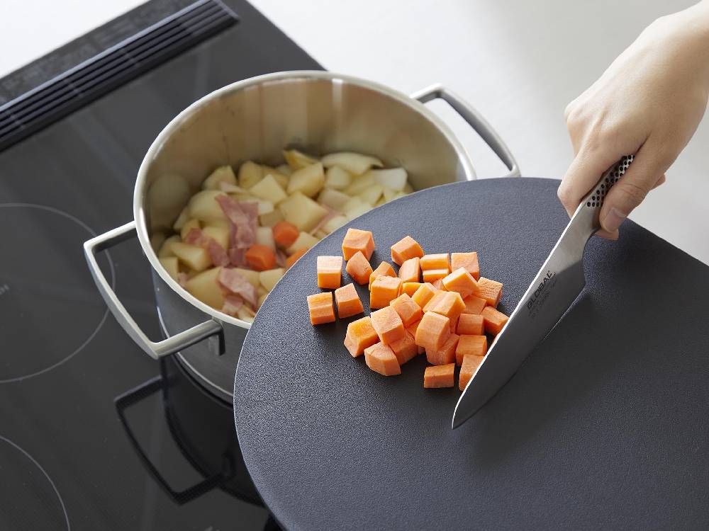 キッチンでタワーのマグネット抗菌ラウンドまな板を使用し、フライパンや野菜などの調理器具が並んでいる様子